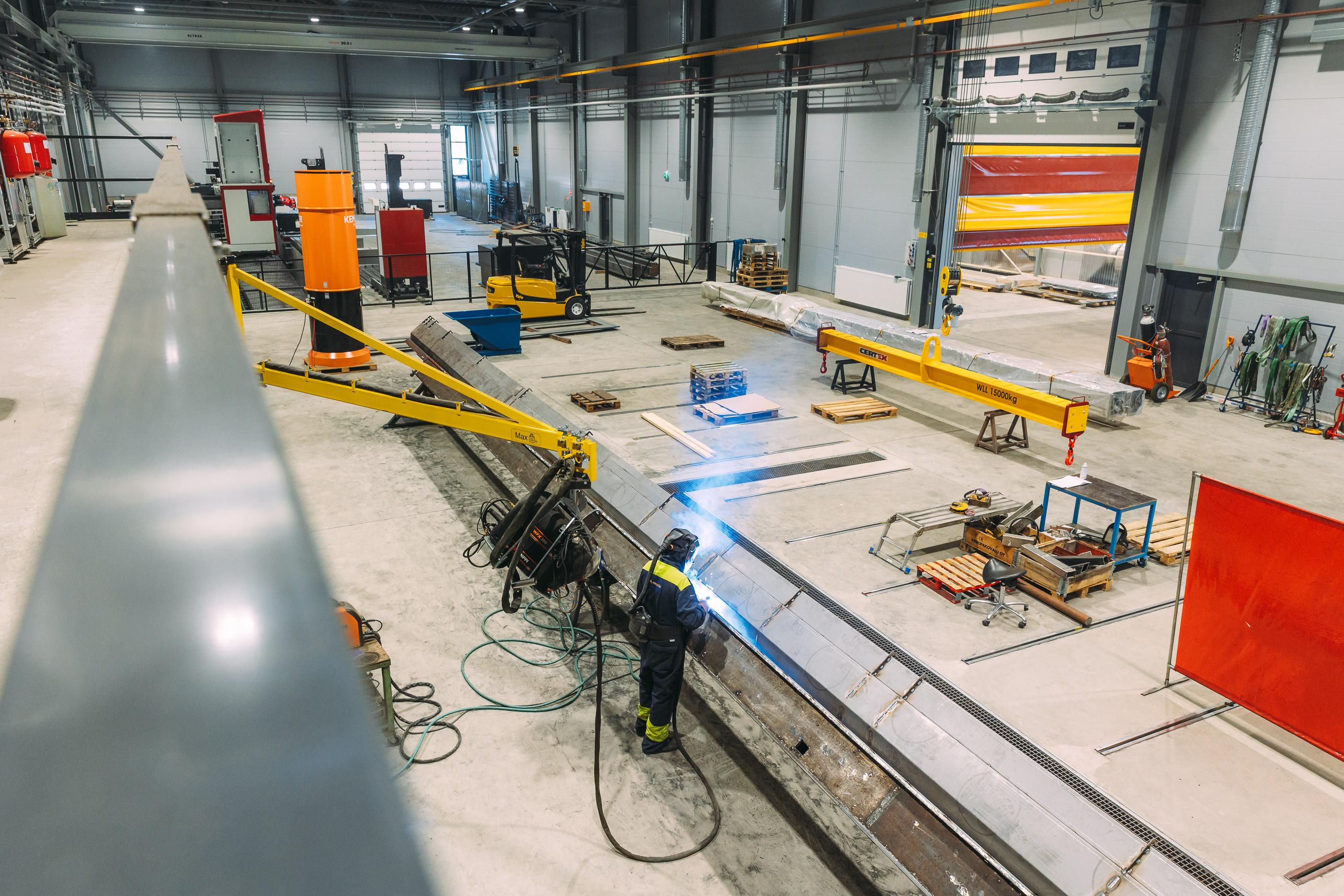 Hitsausammattilainen työskentelee metalliteollisuuden tuotantotiloissa, suojavarusteet päällä ja hitsauslaite kädessä.