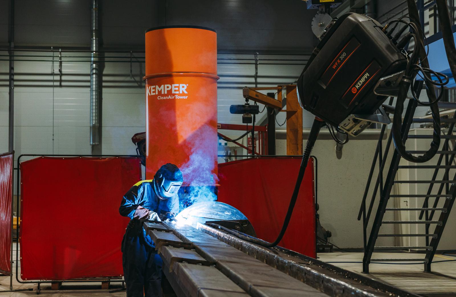 Hitsauksen ammattilainen työskentelemässä metallirakenteen parissa suojavarusteet yllään. Kirkas valokaari valaisee hitsauskohdan.