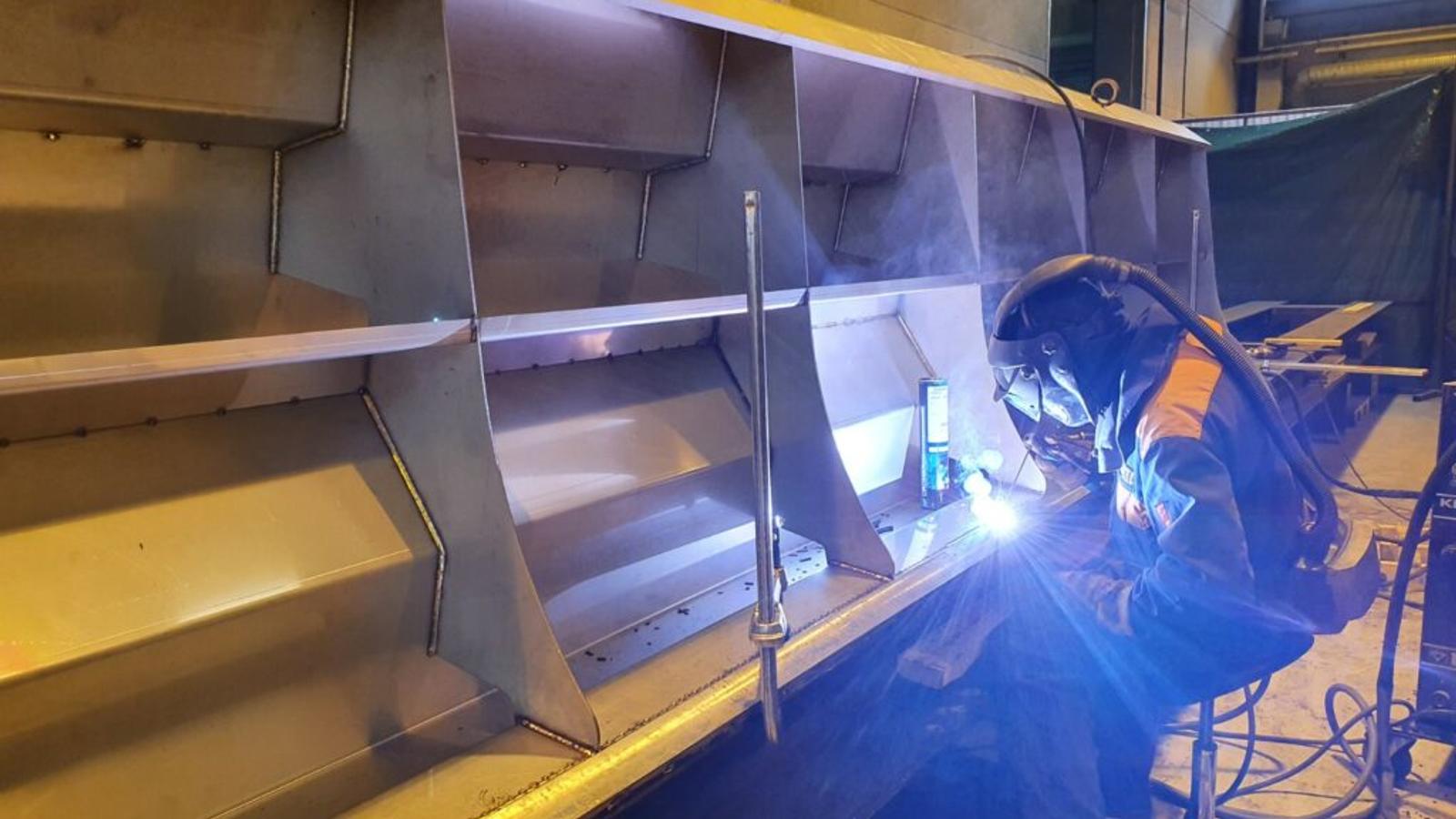 Hitsausprosessi k&auml;ynniss&auml; RTA-Metallin tuotantotiloissa. Hitsaaja ty&ouml;skentelee suuren metallirakenteen parissa yll&auml;&auml;n suojavarusteet.