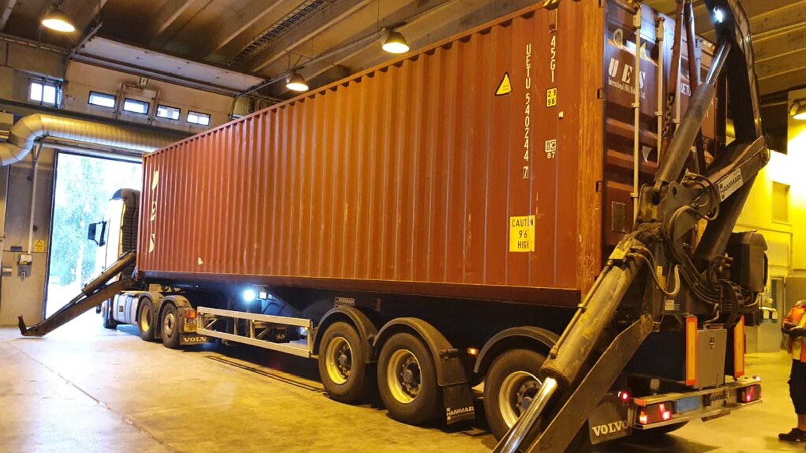 Suuri merikontti lastataan kuljetusautoon RTA-Metallin toimitiloissa. Sivukuormausnosturi varmistaa turvallisen ja tehokkaan lastauksen.